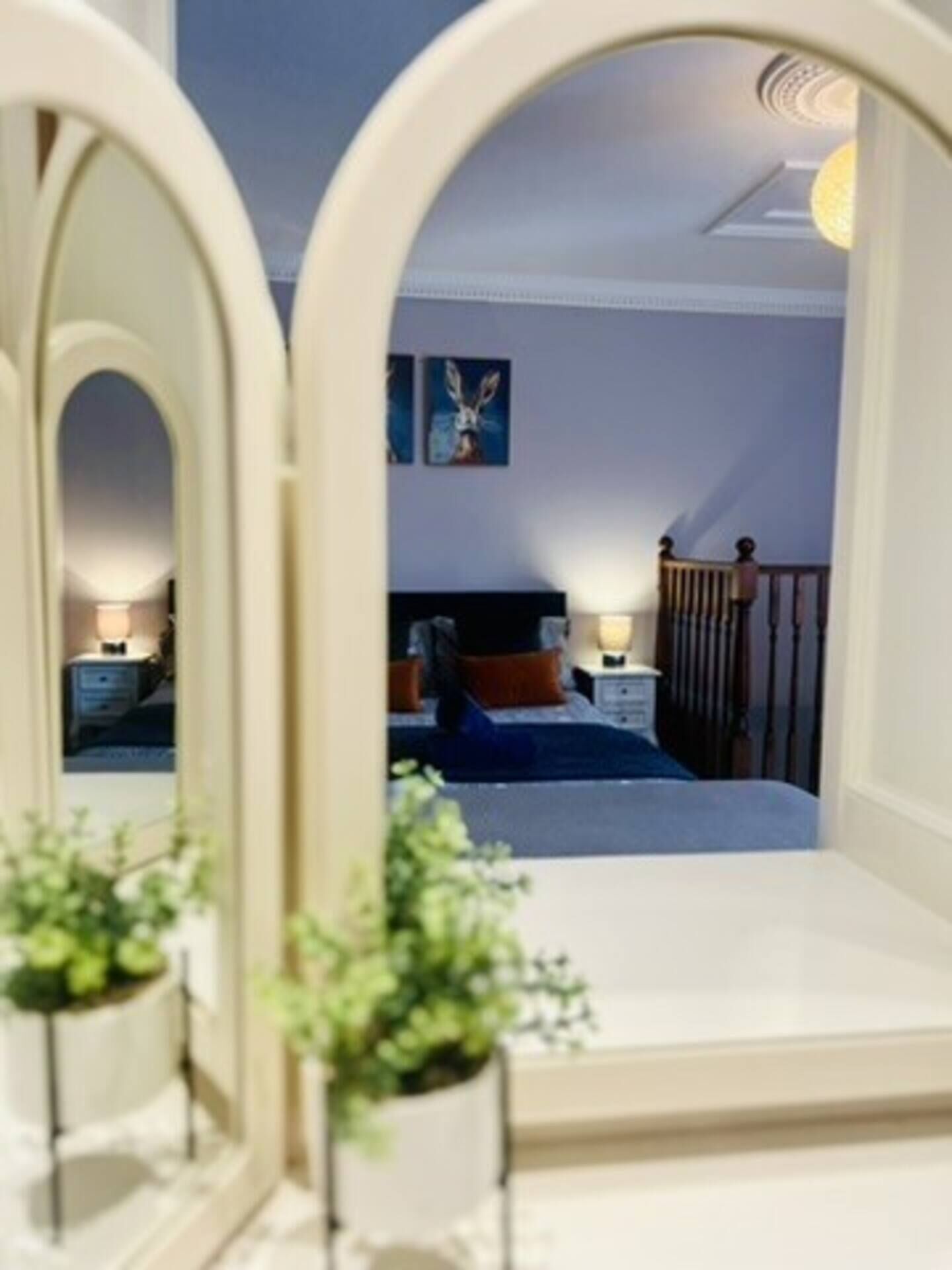 A bedroom with a bed, bedside tables, a nightstand, a lamp, a painting on the wall, and a plant.