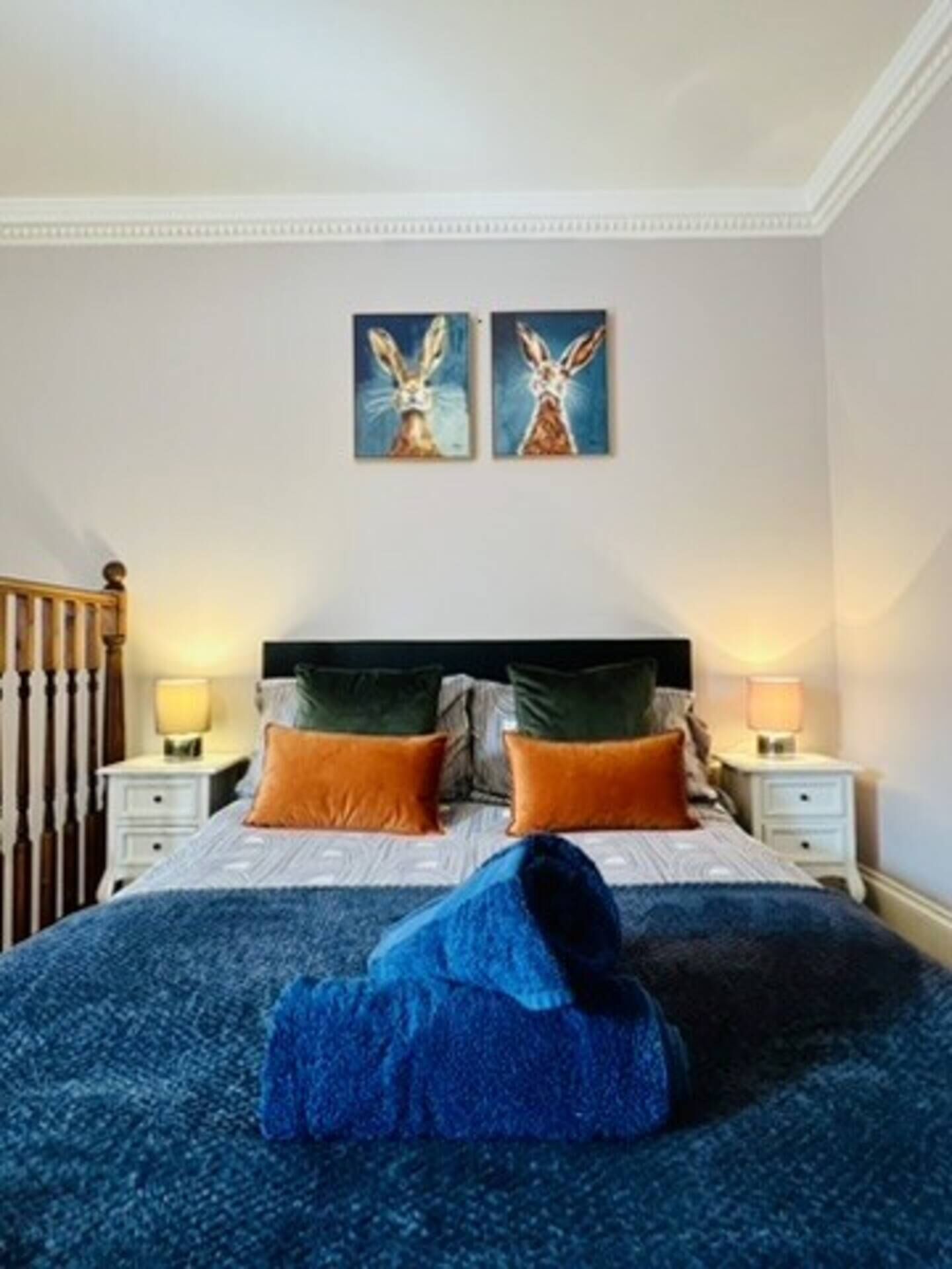 Une chambre à coucher avec un lit double, deux tables de chevet, une tête de lit en bois et deux tableaux accrochés au mur.