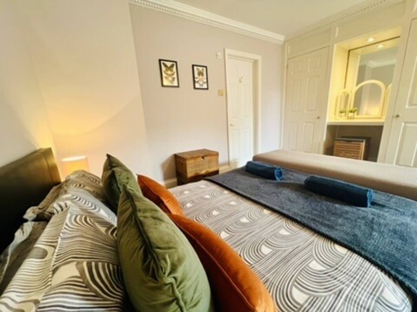 Een slaapkamer met een bed, kussens, een nachtkastje, een spiegel en een kledingkast.