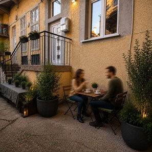 Een terras met een tafel en stoelen, omgeven door potplanten en een trap.