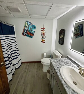 Een badkamer met een gestreept douchegordijn, een toilet, een wastafel en decoratieve muurdecoratie van vissen.