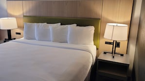 A hotel room with a large bed, two bedside lamps, and a red chair. - IHV-A Country Living (Canton)