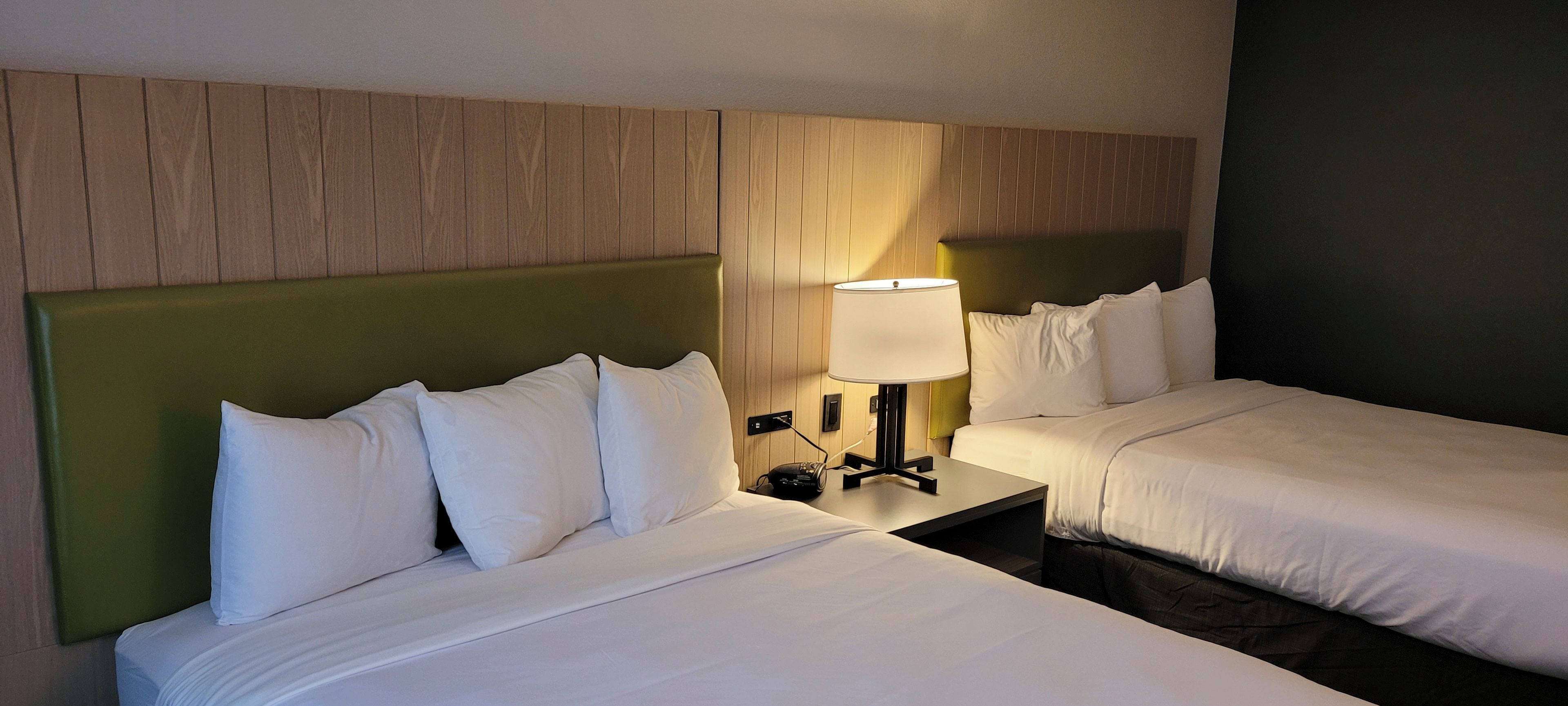 A hotel room with two beds, a nightstand with a lamp, and a wooden headboard.