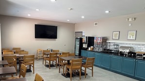 A restaurant with wooden tables and chairs, a kitchen area with a coffee machine, and a flat-screen TV mounted on the wall. - IHV-A Country Living (Canton)