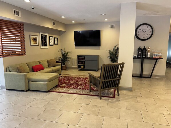 A living room with a sofa, a red rug, a wooden chair, a flat-screen TV, a clock, and a small table with bottles.