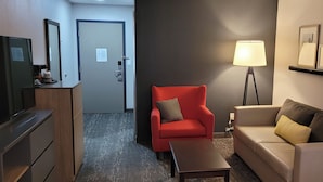 A hotel room with a red armchair, a beige sofa, a small table, a lamp, and a desk with a mirror. - IHV-A Country Living (Canton)