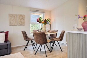 A dining area with a round table, four chairs, and a vase of flowers. - 4P Modern Chalet with Private Sauna - Fenced Garden in a Forest Area - BBQ (Putten)