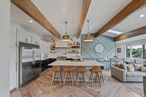 A modern kitchen with a central island, bar stools, and a dining area with a sofa.
