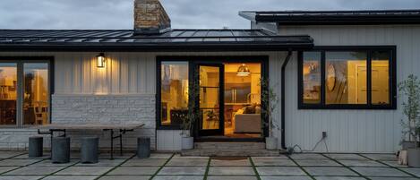 Une maison moderne avec une façade en pierre, de grandes fenêtres et un patio aménagé avec une table et des chaises.