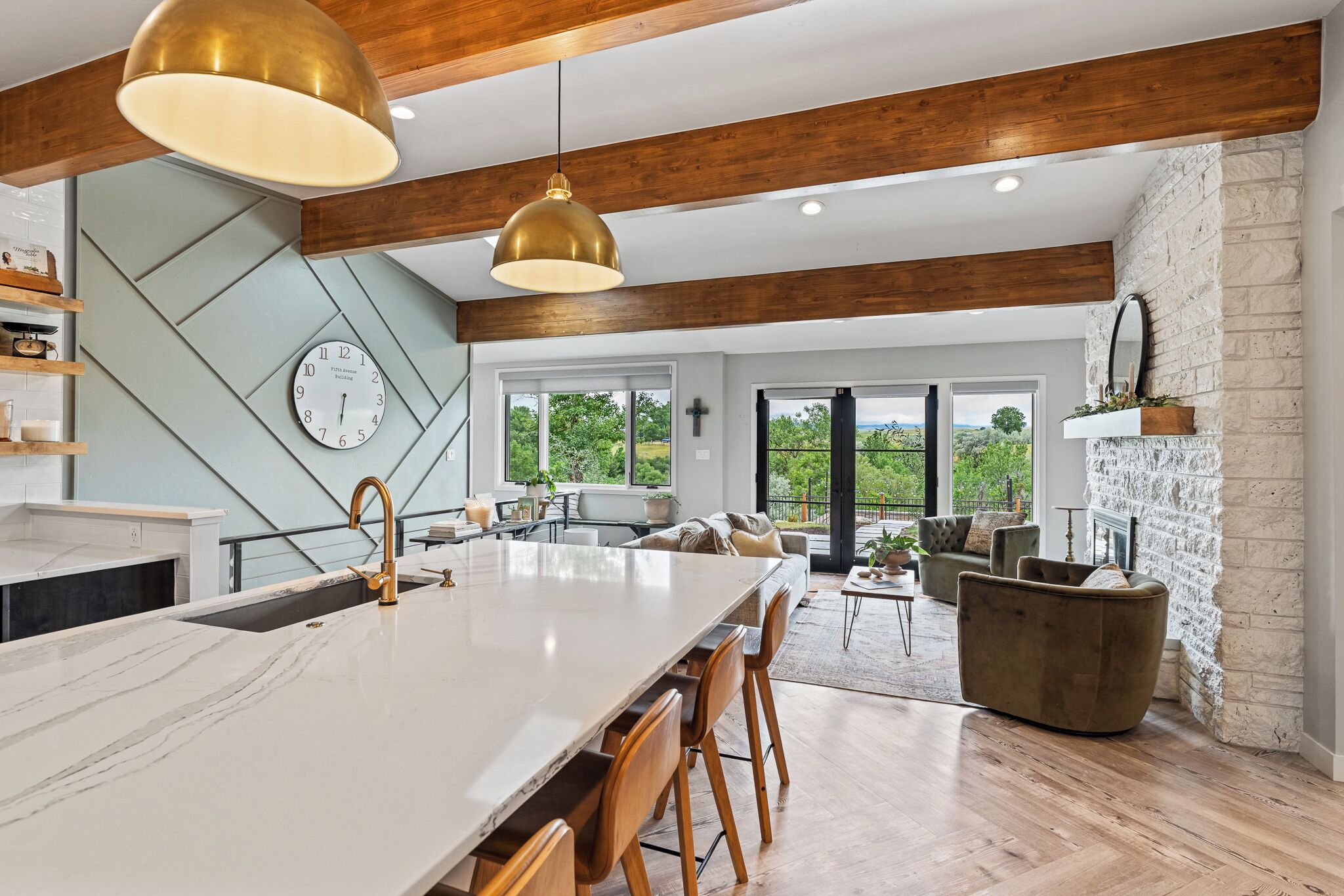 A modern kitchen with a large island, wooden beams, and a view of the outdoors.