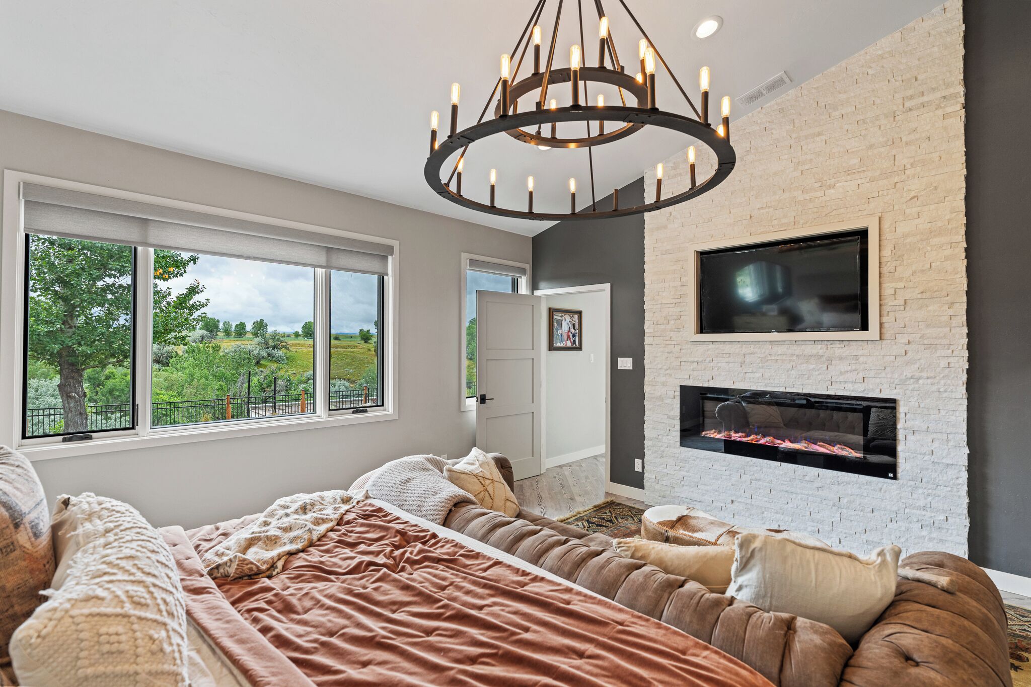 Un dormitorio moderno con una cama grande, una chimenea y vistas a un paisaje verde a través de amplios ventanales.