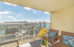 A balcony with a city view, a wicker sofa, a table, and a bottle of wine. - Ocean-diamond Head Views From Island Colony Condo Short Walk to Waikiki Beach (Honolulu)