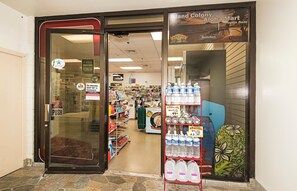 A store entrance with a glass door, shelves stocked with bottled water, and a sign indicating the store is open 8am. - Ocean-diamond Head Views From Island Colony Condo Short Walk to Waikiki Beach (Honolulu)