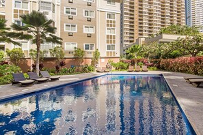 A swimming pool with lounge chairs and palm trees, surrounded by a landscaped garden and high-rise buildings. - The Cove Waikiki Condo W/full Kitchen by the Beach and Free Parking/wifi (Honolulu)