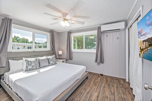 Un dormitorio con cama, ventilador de techo, dos ventanas y aire acondicionado.