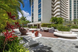 A modern hotel courtyard with outdoor seating, palm trees, and a large building in the background. - Mountain-city Views Condo at Allure W/parking (Honolulu)