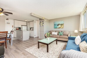 A modern living room with a blue sofa, a coffee table, and a dining area with a wooden table and chairs. - Mountain & Golf Course Views Family Island Colony Condo & Lots of Amenities (Honolulu)