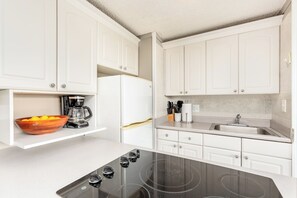 A modern kitchen with white cabinetry, a black stovetop, and a bowl of fruit on the counter. - Mountain & Golf Course Views Family Island Colony Condo & Lots of Amenities (Honolulu)
