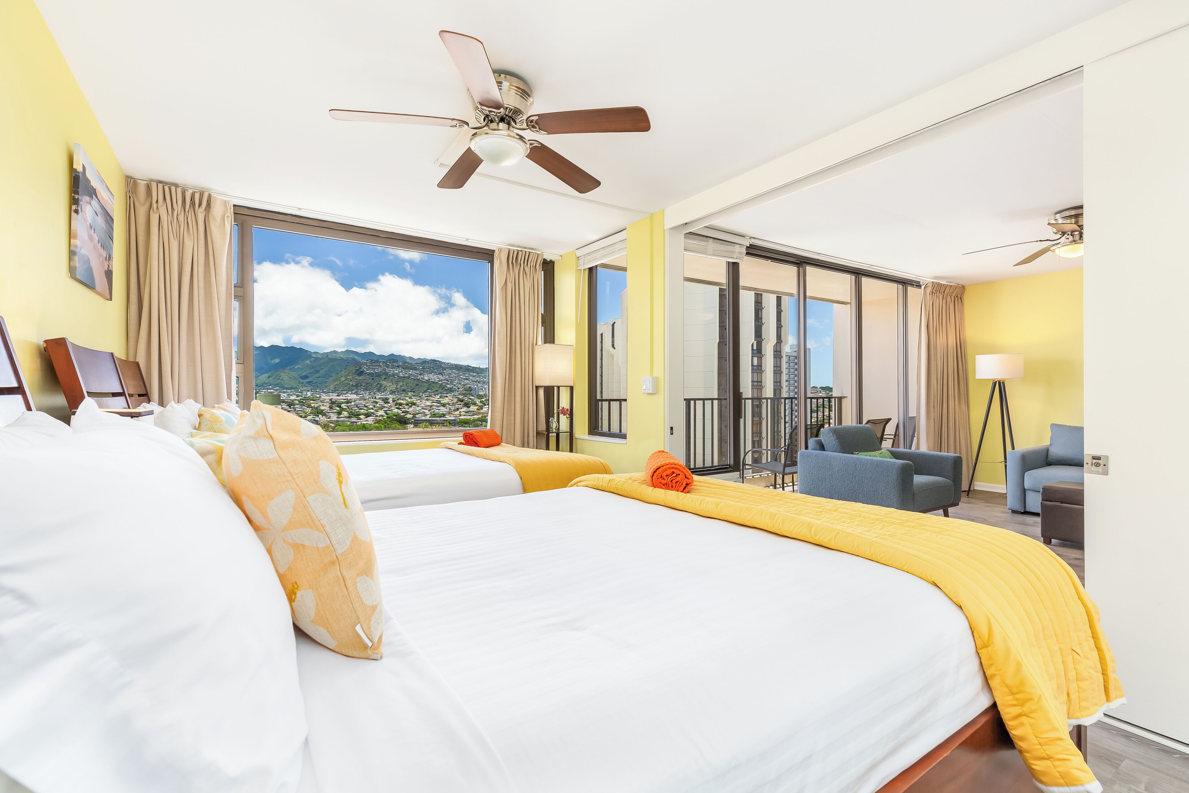 A hotel room with two beds, a balcony, and a view of a cityscape.