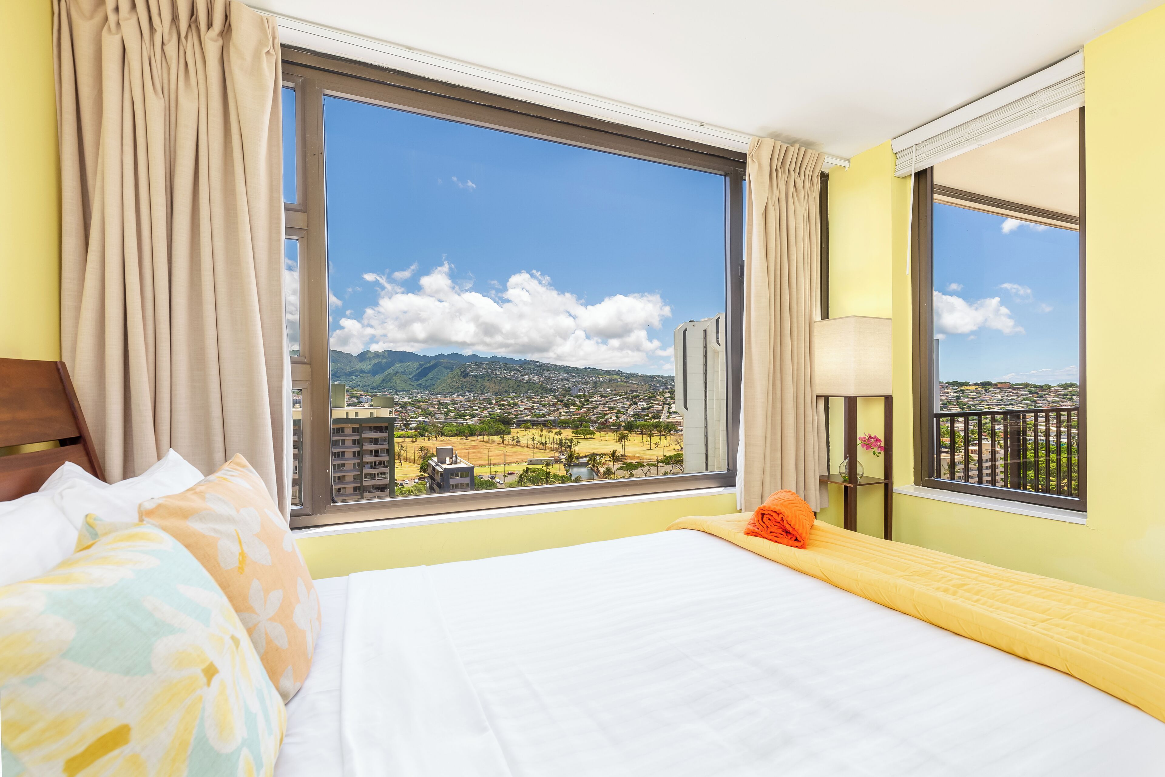 A hotel room with a large window offering a view of a cityscape and mountains.