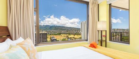 A hotel room with a large window offering a view of a cityscape and mountains.