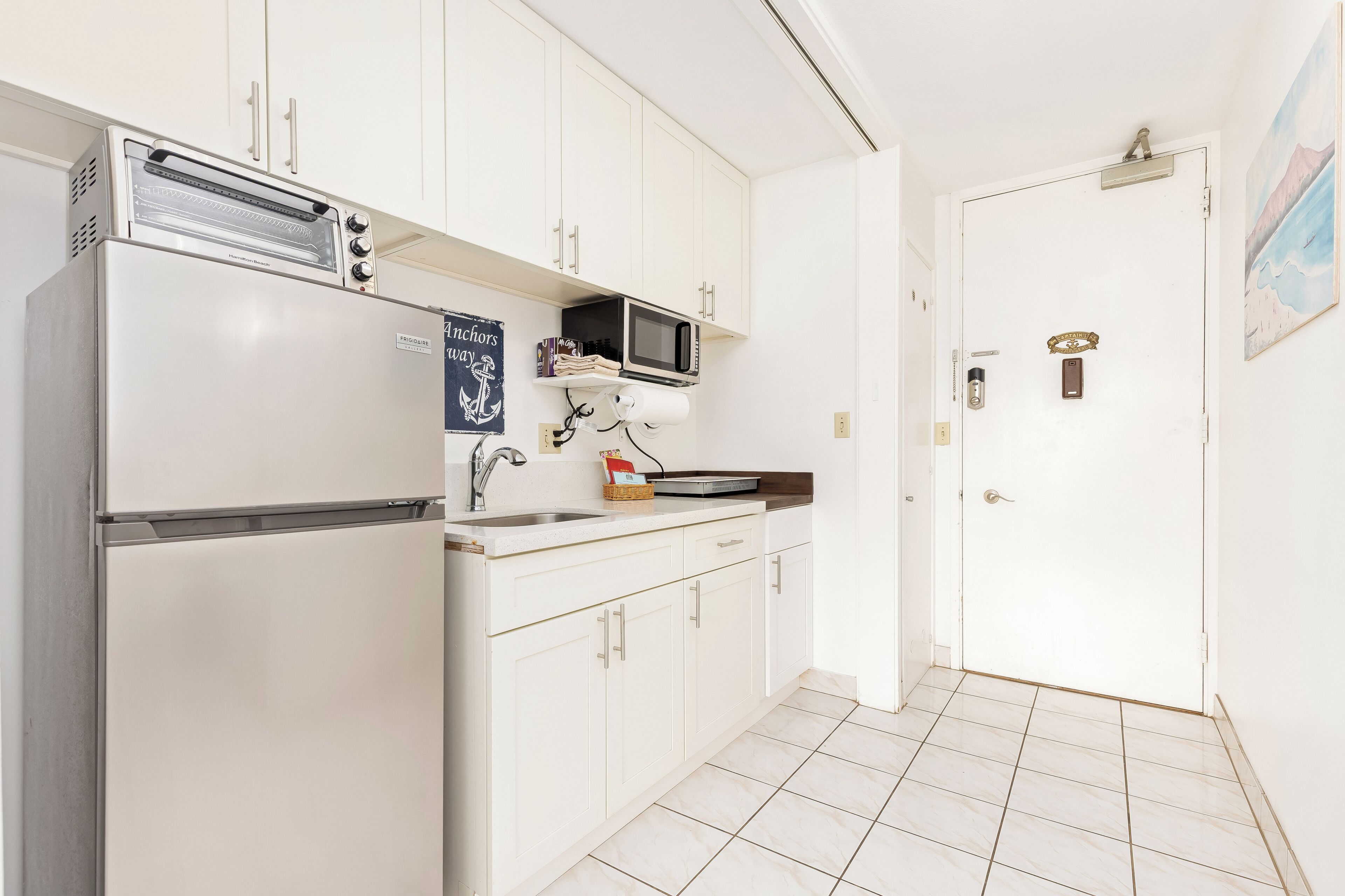 A kitchen with white cabinets, a built-in microwave, a stainless steel refrigerator, and a tiled floor.