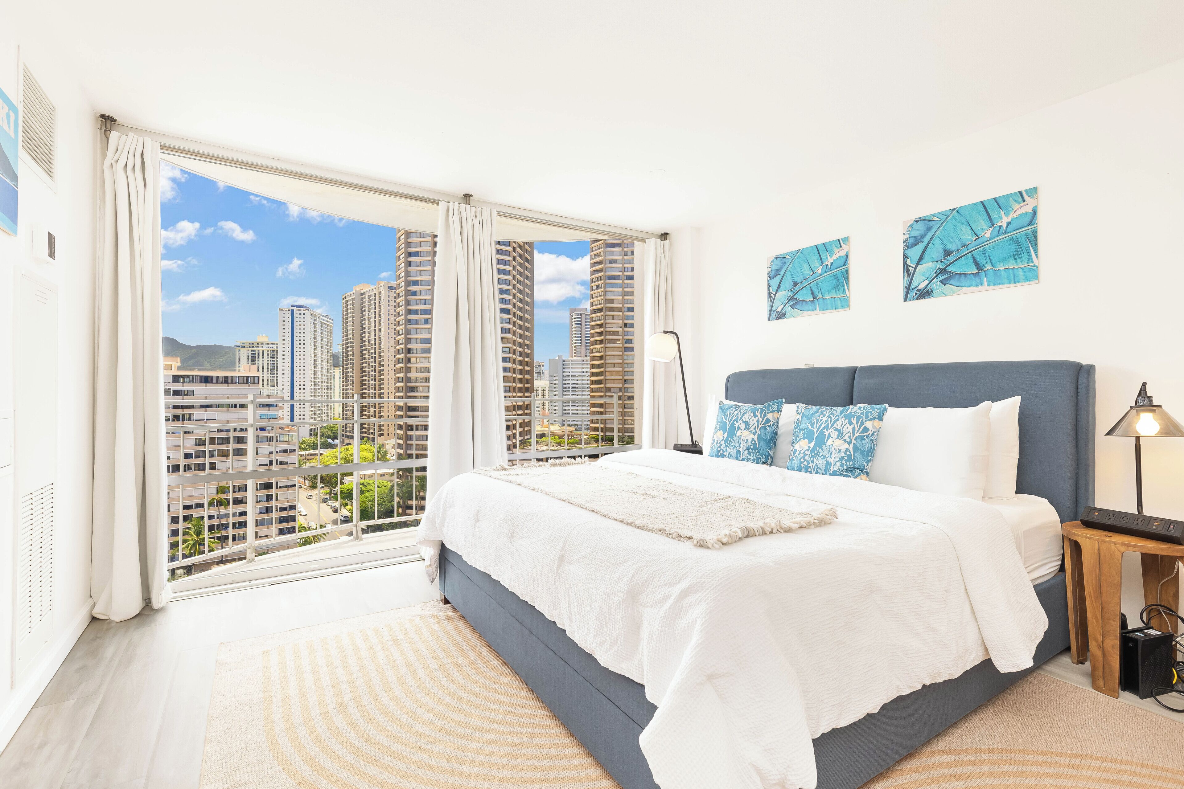 A bedroom with a large window, a bed, and artwork on the wall.