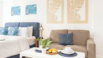 Quarto de hotel com cama, sofá, mesa de centro com itens de café da manhã e arte nas paredes.