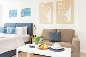 Quarto de hotel com cama, sofá, mesa de centro com itens de café da manhã e arte nas paredes.