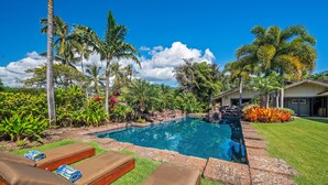 A swimming pool with lounge chairs, surrounded by tropical plants and a house.