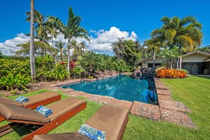 A swimming pool with lounge chairs, surrounded by tropical plants and a house.