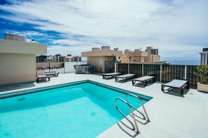 A rooftop pool with lounge chairs and a view of the cityscape. - Fairway Villa in the Heart of Waikiki by the Beach W/rooftop Pool & Amenities (Honolulu)