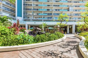 Ein Hotel mit mehreren Balkonen, einem angelegten Garten mit tropischen Pflanzen und einem Holzsteg.