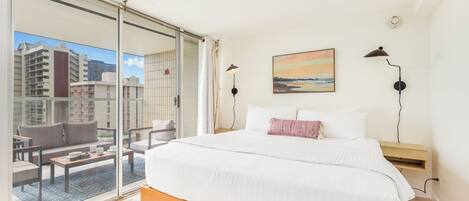 A hotel room with a large bed, a view of the city through floor-to-ceiling windows, a painting on the wall, and a balcony with seating.