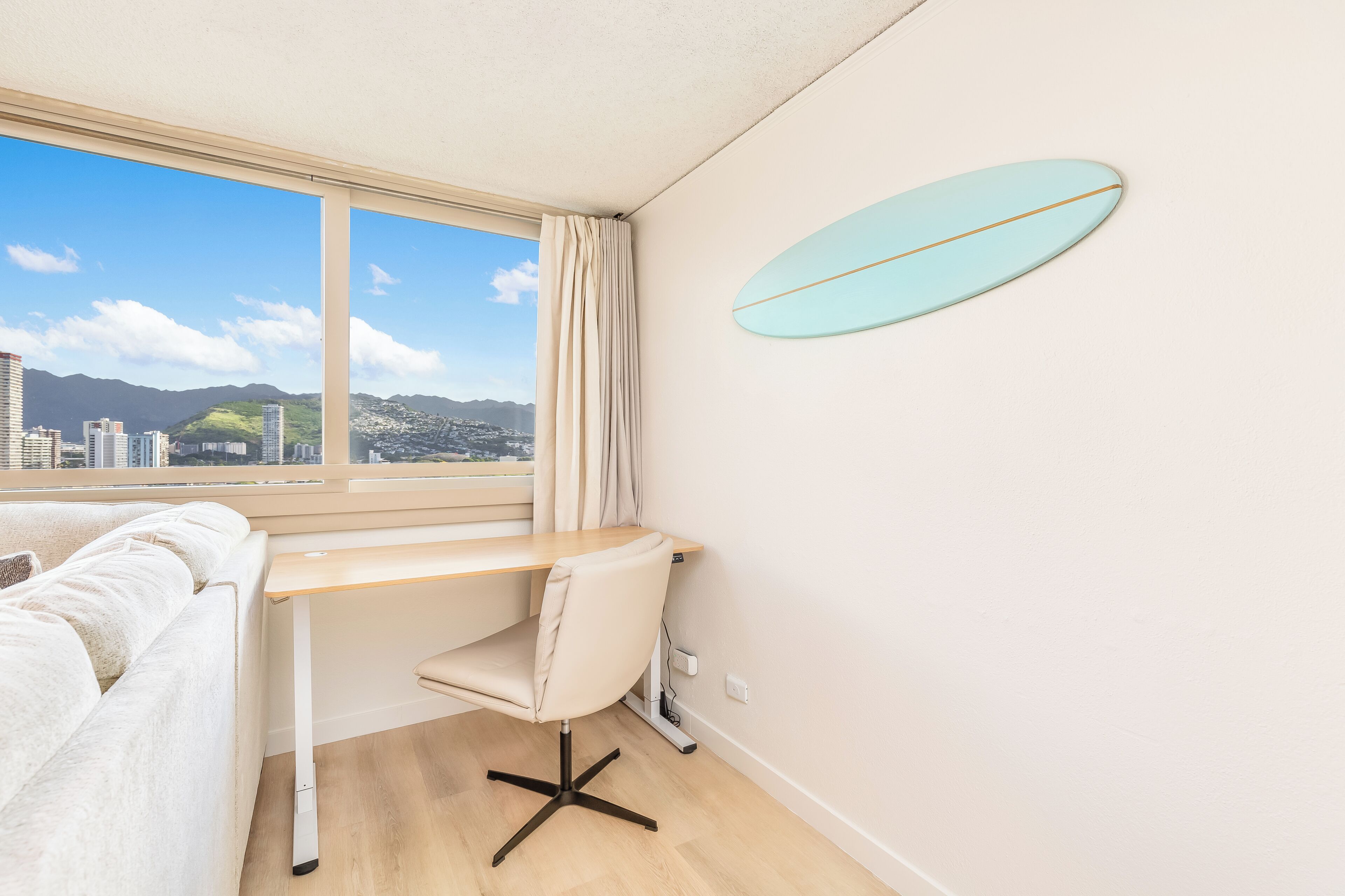 Une chambre d’hôtel moderne avec une grande fenêtre, un bureau, une chaise et une planche de surf accrochée au mur.