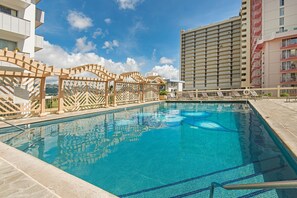 Une piscine dotée d’une terrasse en bois et de chaises longues, entourée d’immeubles de grande hauteur.