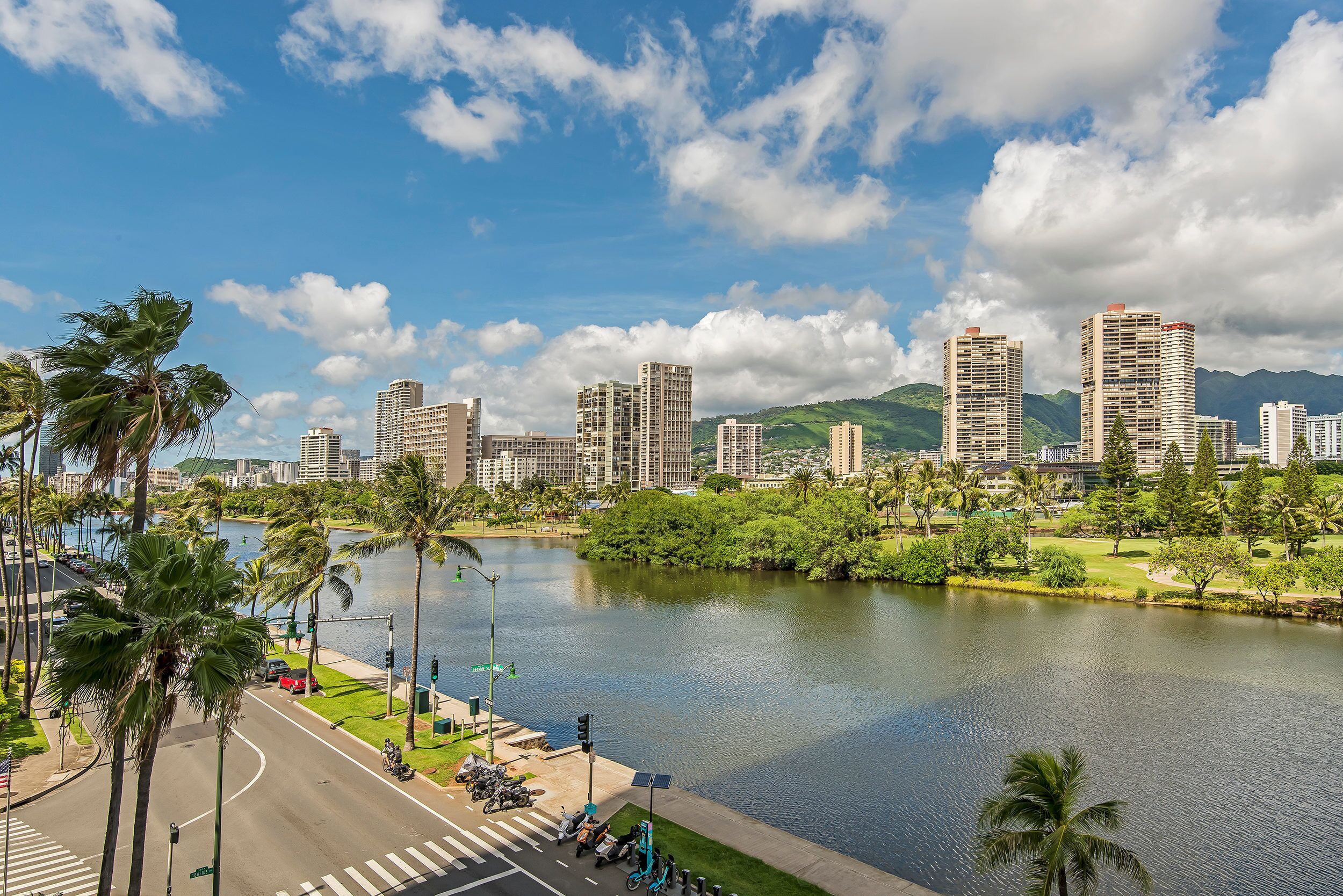 A cityscape with high-rise buildings, a river, and palm trees.