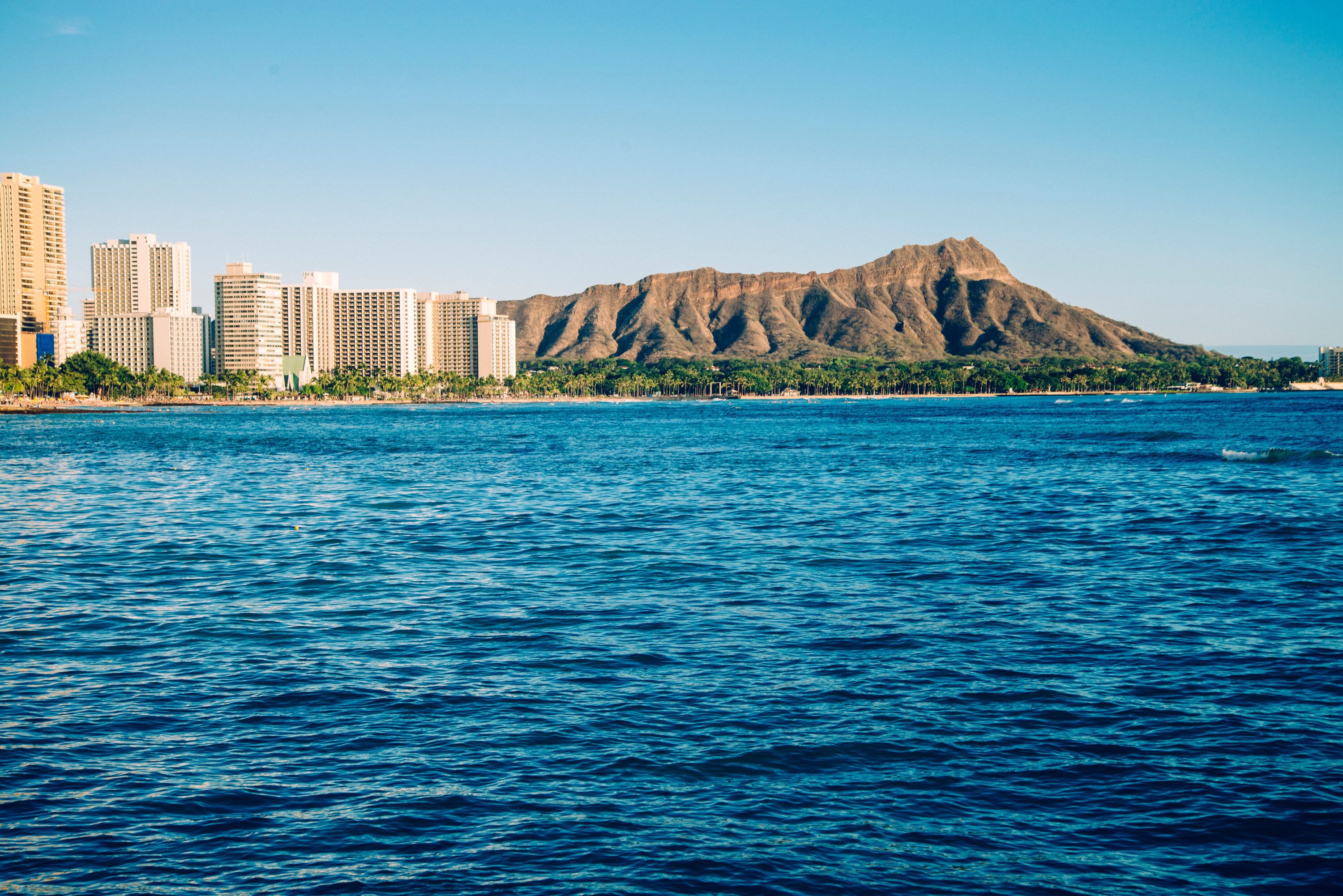 A coastal cityscape with a prominent mountain in the background and a body of water in the foreground.