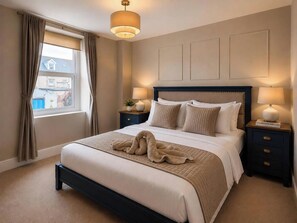 A bedroom with a bed, bedside tables, a lamp, a window with curtains, and a view of buildings outside. - Number 8 (Llandudno)