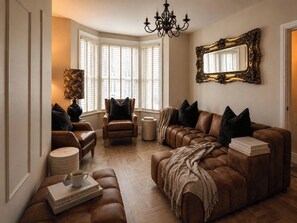 A living room with leather sofas, a chandelier, a large mirror, and books on a coffee table. - Number 8 (Llandudno)