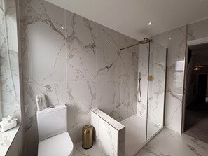 A modern bathroom with a glass-enclosed shower, a white toilet, and a marble-tiled wall. - Number 8 (Llandudno)
