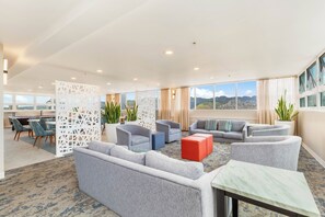 A spacious lounge area with grey sofas, armchairs, and a red ottoman. There is a decorative white partition and potted plants. - Ocean-diamond Head Views Condo at Pacific Monarch Hotel Steps to the Beach (Honolulu)