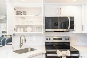 Eine moderne Küche mit weißen Schränken, einer Edelstahlspüle, einem Backofen, einer Mikrowelle und einem Essbereich mit einem Stuhl.