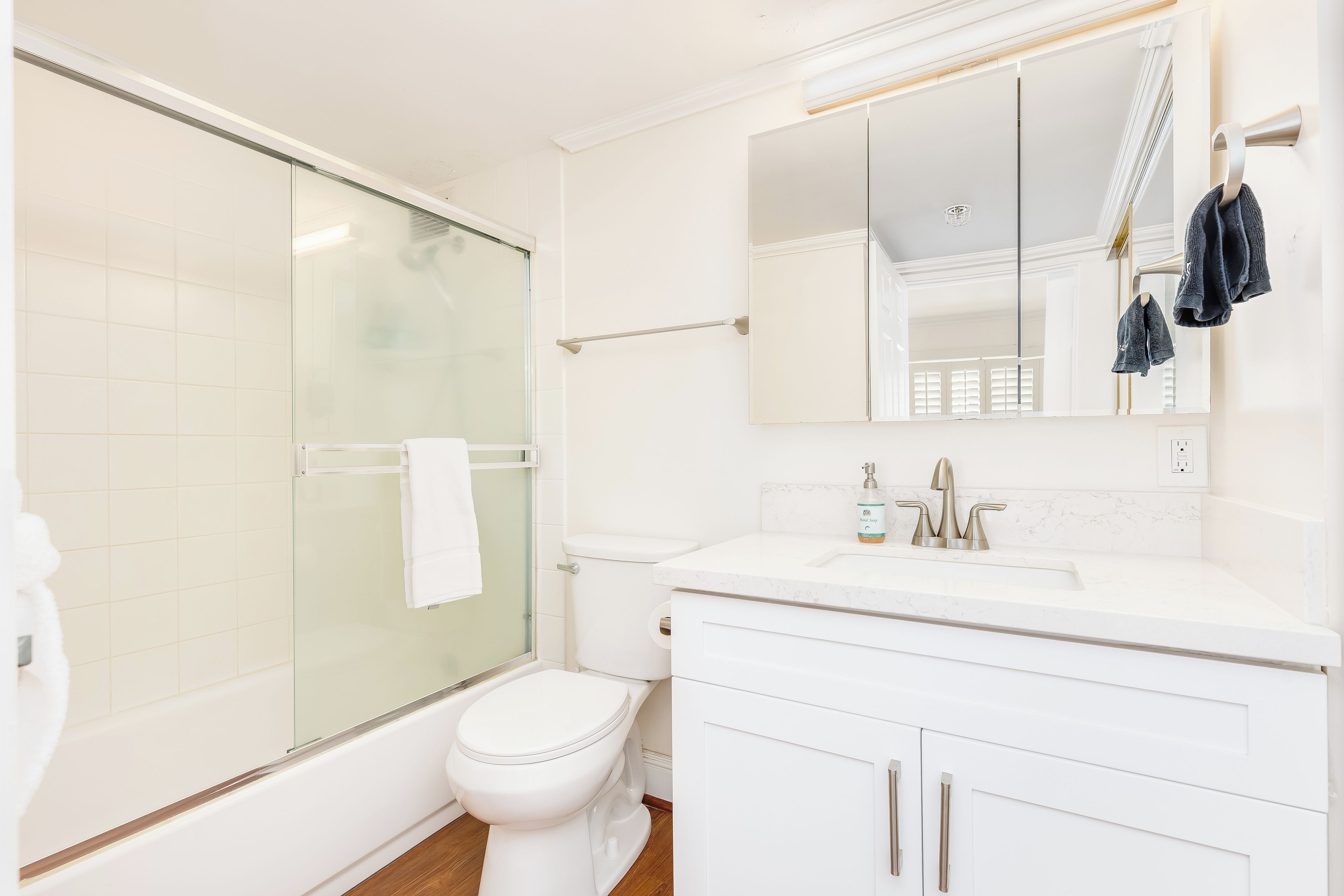 Een moderne badkamer met een glazen douchecabine, een wit toilet, een wastafel met spiegel erboven en een handdoekrek met handdoeken.