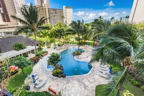 A resort with a central swimming pool, palm trees, and a stone patio area. - Luxurious Ocean View Panoramic PH at The Watermark W/spectacular Amenities (Honolulu)
