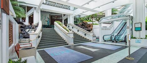A modern hotel lobby with a staircase, escalators, and a seating area.