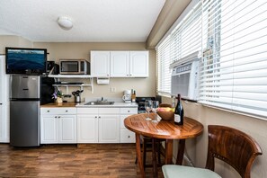 A compact kitchen with white cabinets, a stainless steel refrigerator, a microwave, and a small dining area with a wooden table and chairs. - Hawaiian Relaxing Vacation by Beach W/full Kitchen Short Walk to Dine & Shop (Honolulu)