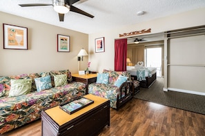 A hotel room with a sofa, a bed, a wooden coffee table, a lamp, and a ceiling fan. - Hawaiian Relaxing Vacation by Beach W/full Kitchen Short Walk to Dine & Shop (Honolulu)