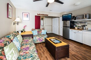 A compact living space with a sofa, a small table, a kitchenette, and a ceiling fan. - Hawaiian Relaxing Vacation by Beach W/full Kitchen Short Walk to Dine & Shop (Honolulu)