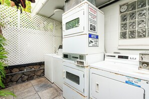 Une buanderie équipée de machines à laver et de sèche-linge superposés, un avis indiquant les heures d’utilisation de la buanderie et un panneau signalant la présence d’une vidéosurveillance 24 heures sur 24.